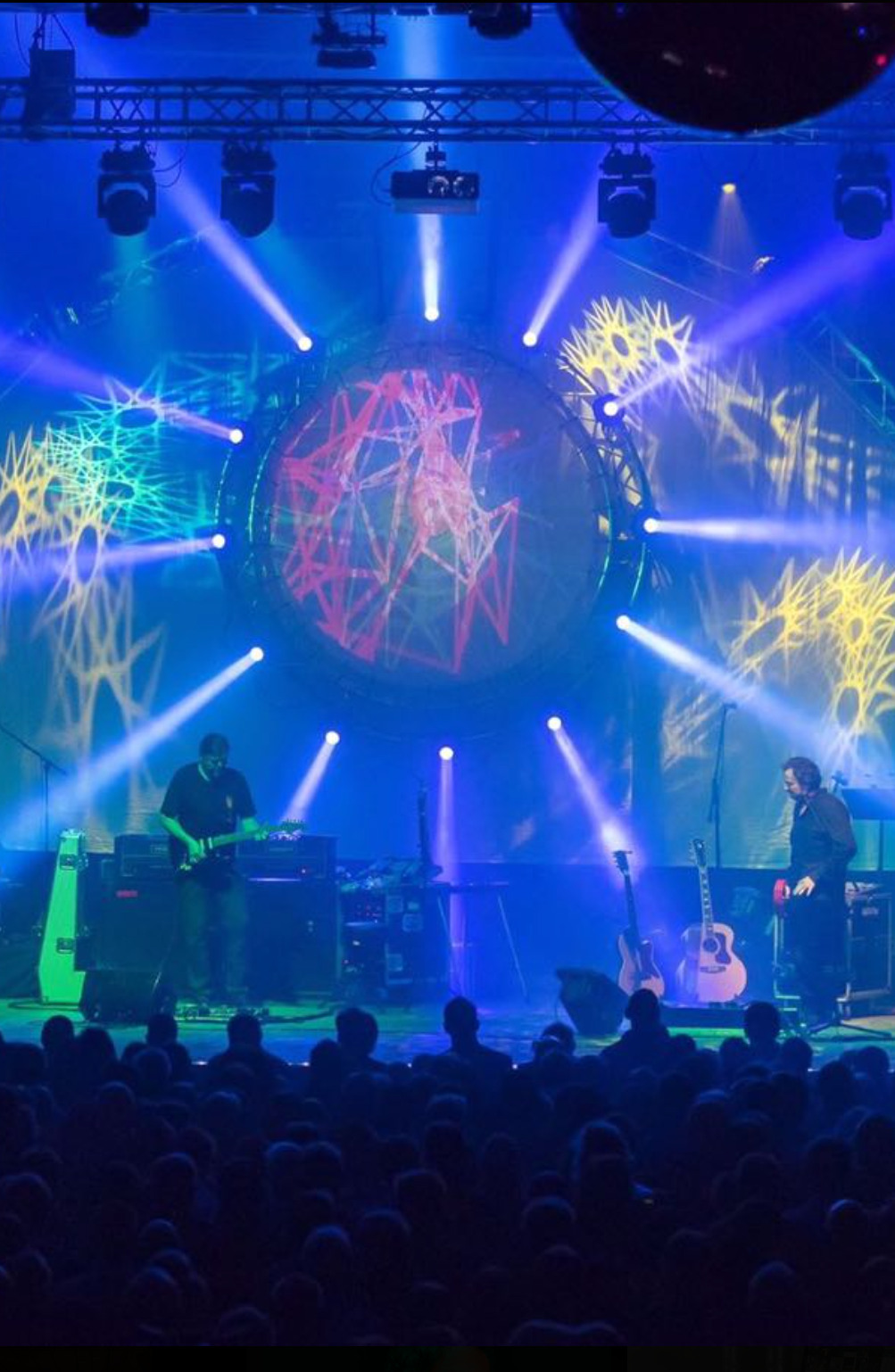Eine Band steht auf der Bühne in blauem Scheinwerferlicht.