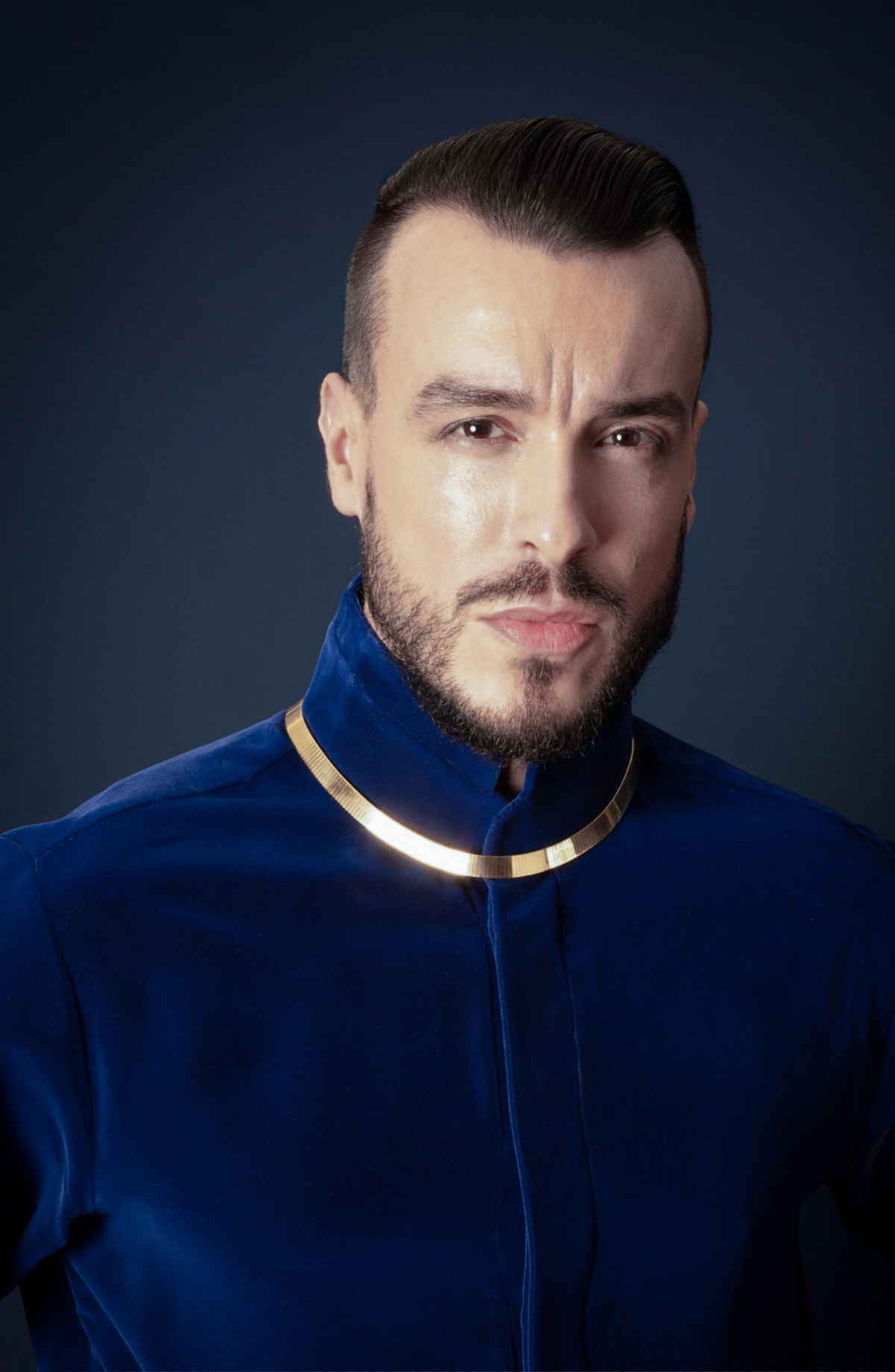 Musiker Cem Adrian mit blauem Oberteil vor dunklem Hintergrund