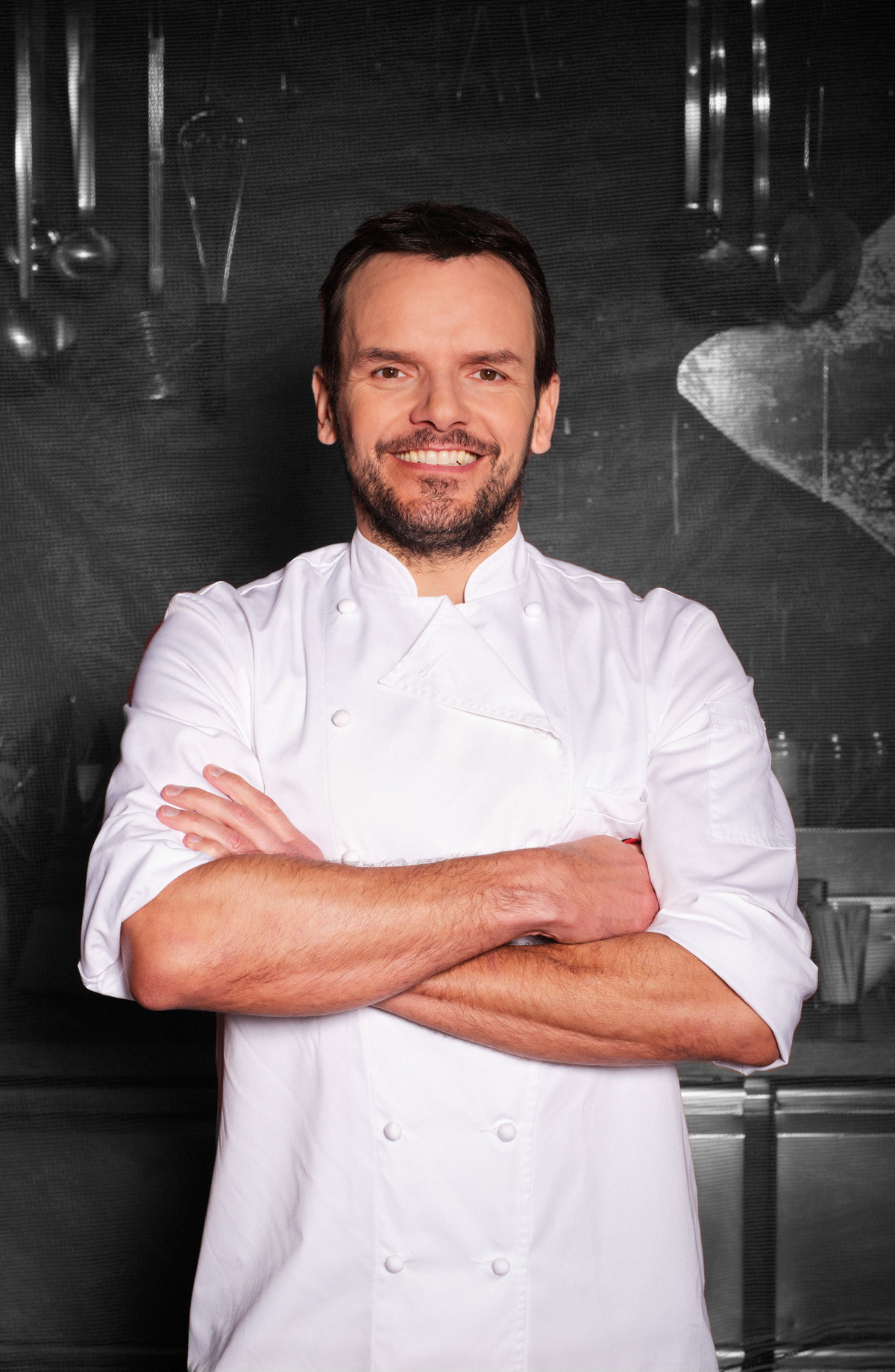 TV-Koch Steffen Henssler in weißer Kochjacke vor einem grauen Hintergrund