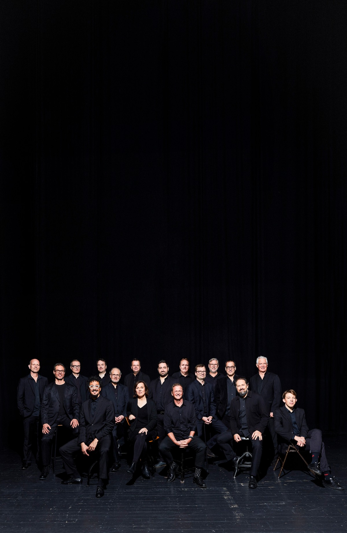 Bandmitglieder in dunkelblauer Kleidung vor dunklem Hintergrund sitzend 