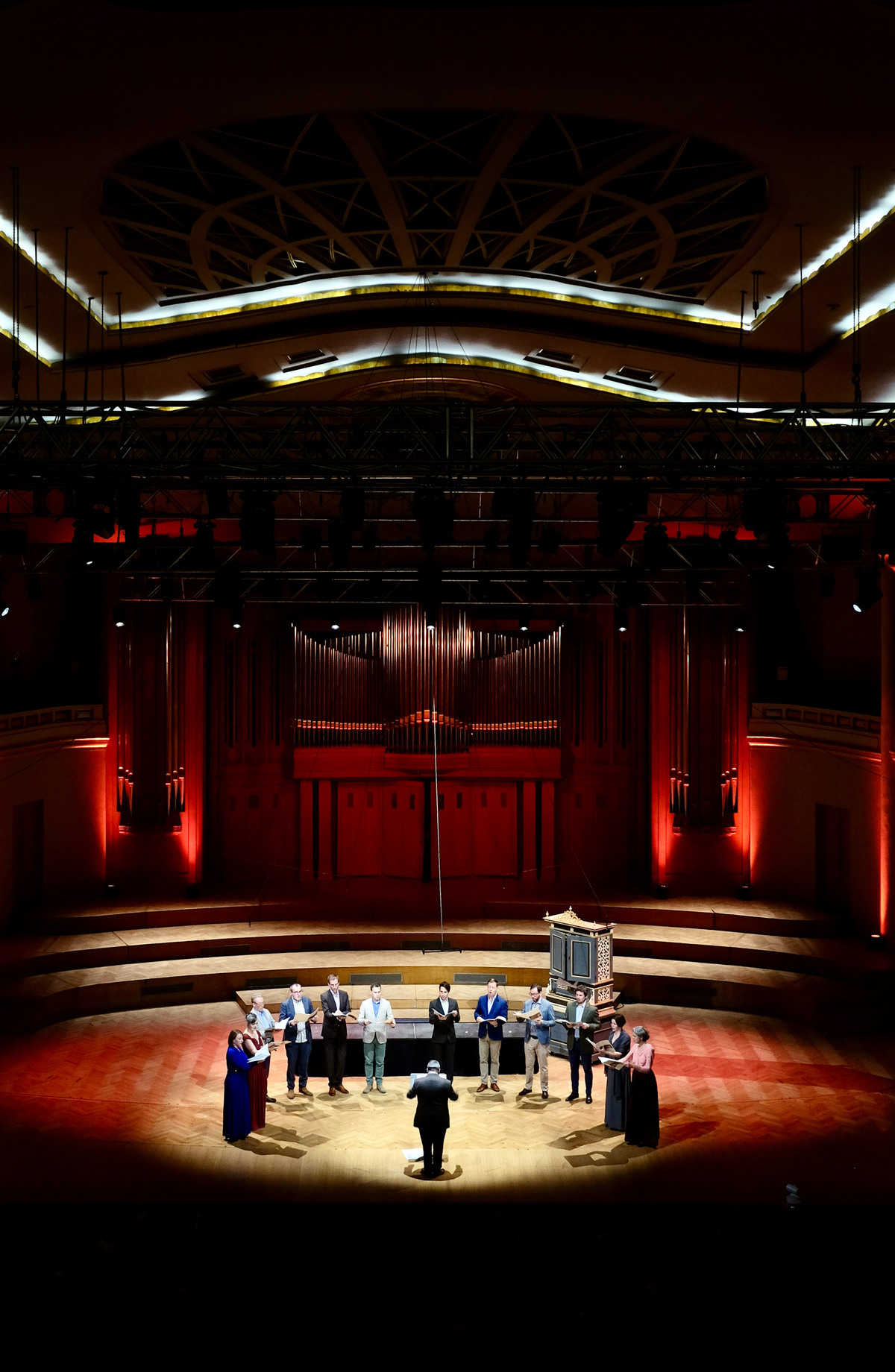 Musiker:innen im Halbkreis stehend in einem großen Konzertsaal