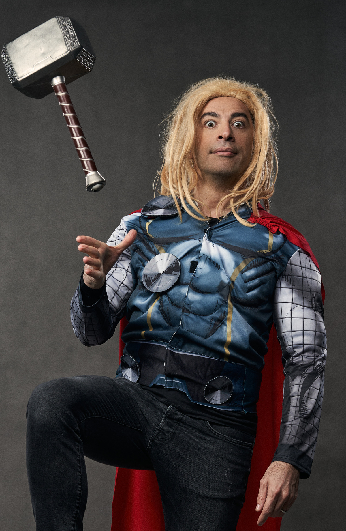 Bülent Ceylan in einem Superheldenkostüm, das dem von Thor ähnelt, mit einem Hammer, der so aussieht als würde er in der Luft schweben. Bülent Ceylan hat einen überraschten Gesichtsausdruck und blonde, zerzauste Haare.
